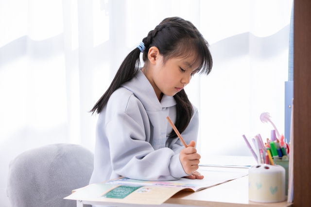女の子が机に向かい、鉛筆を持って一人で課題に取り組んでいる場面