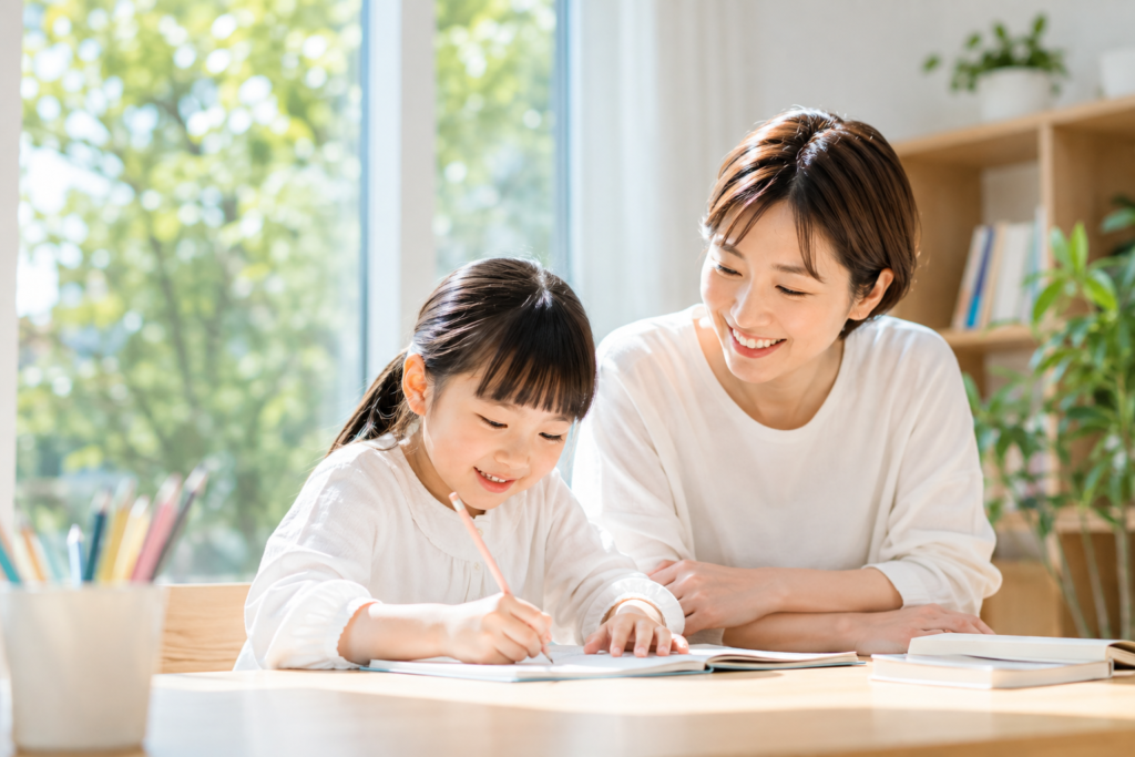 保護者が隣に座り、子どもが自分で宿題を進める様子を見守っている場面