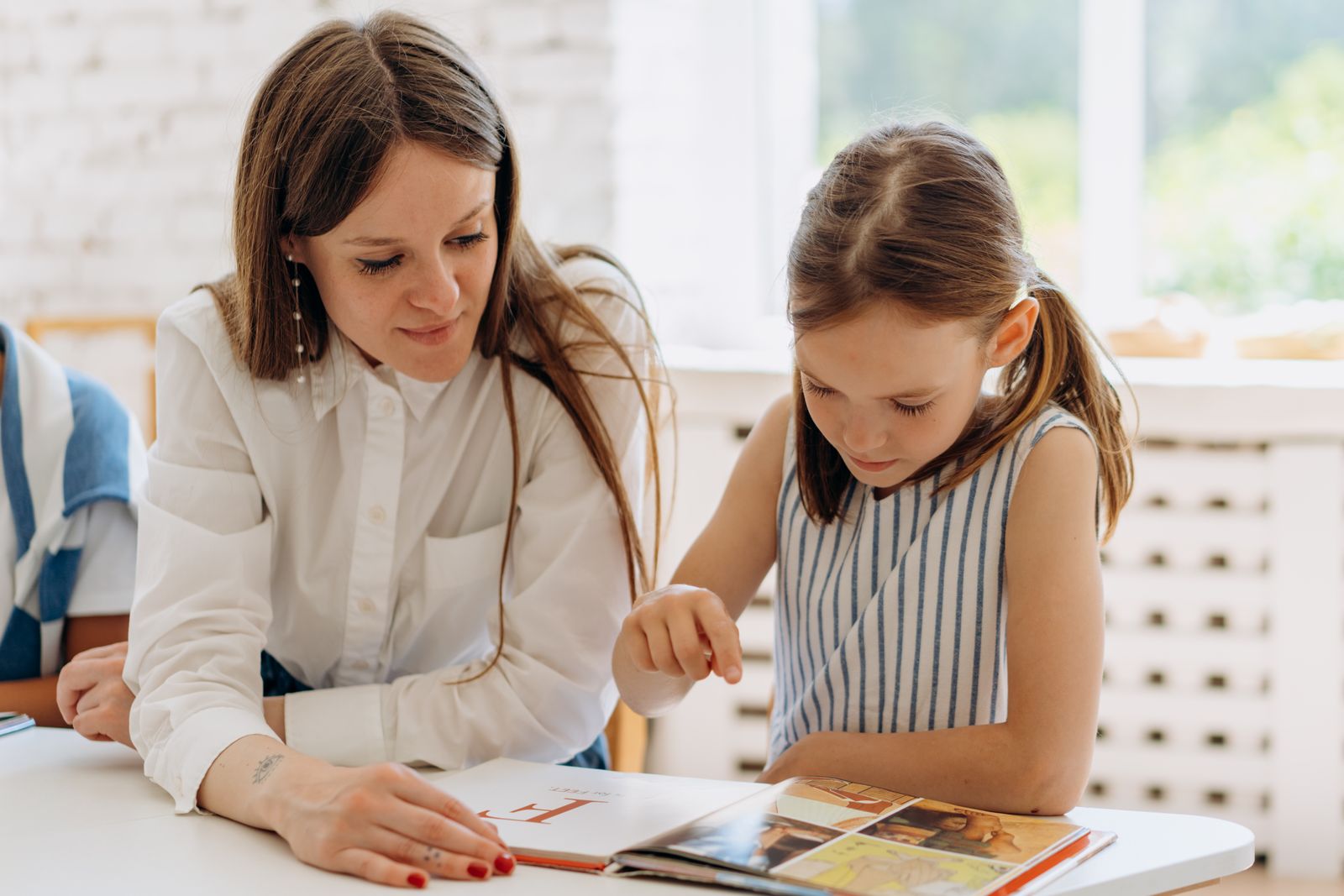 A teacher and a student reading a book together at a table