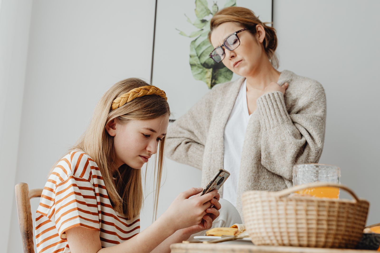 A teenager and a parent sitting together at a kitchen table looking at a phone