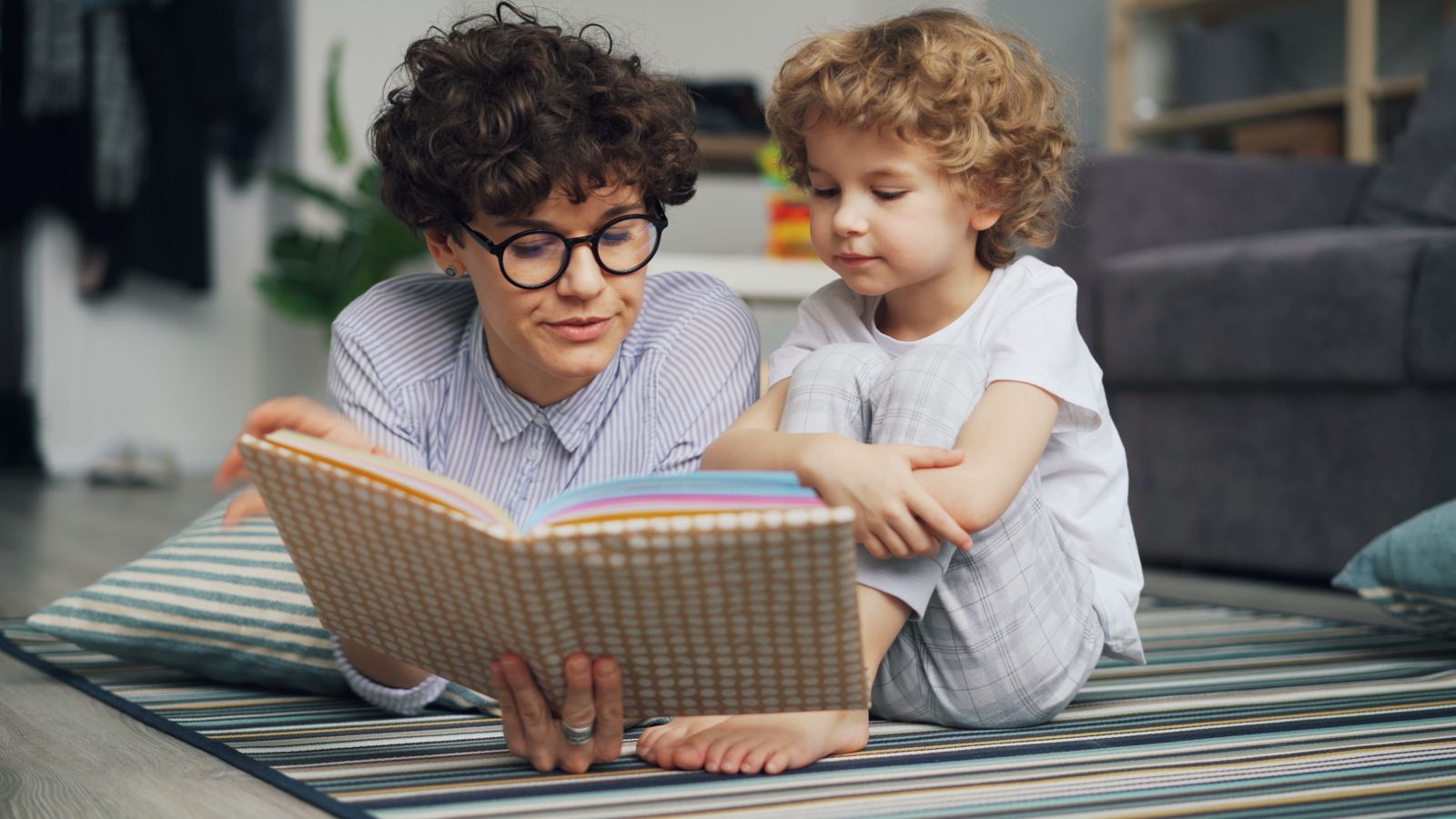 A parent and child reading a picture book together at a sunny kitchen table