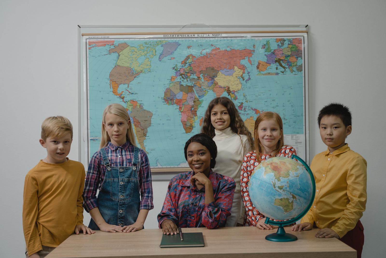 世界地図と地球儀を前に並ぶ、さまざまな国籍の子どもたちのイメージ