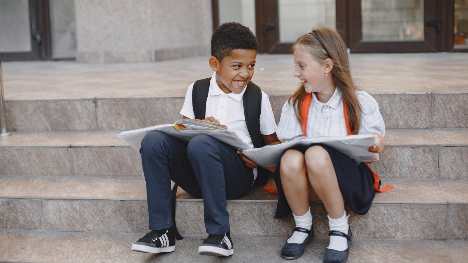 Two children with school bags chatting on some steps