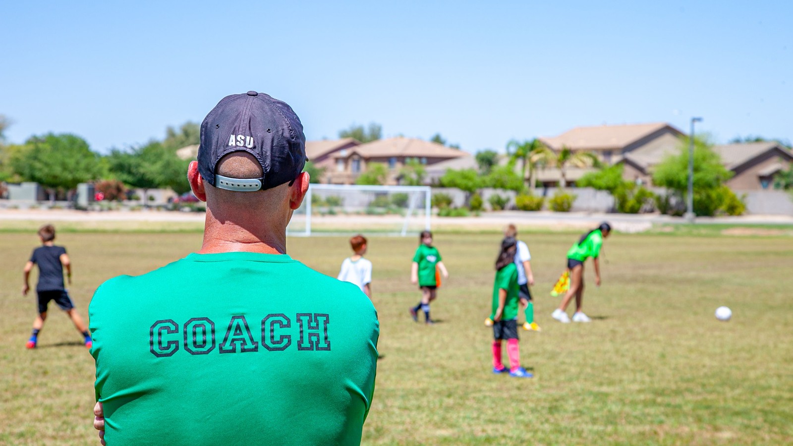 屋外のグラウンドでサッカーの練習をする子どもたちとコーチ