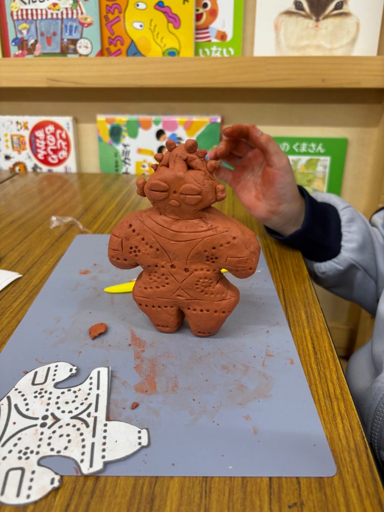 粘土でつくった土偶の作品に、子どもが手を伸ばしている様子