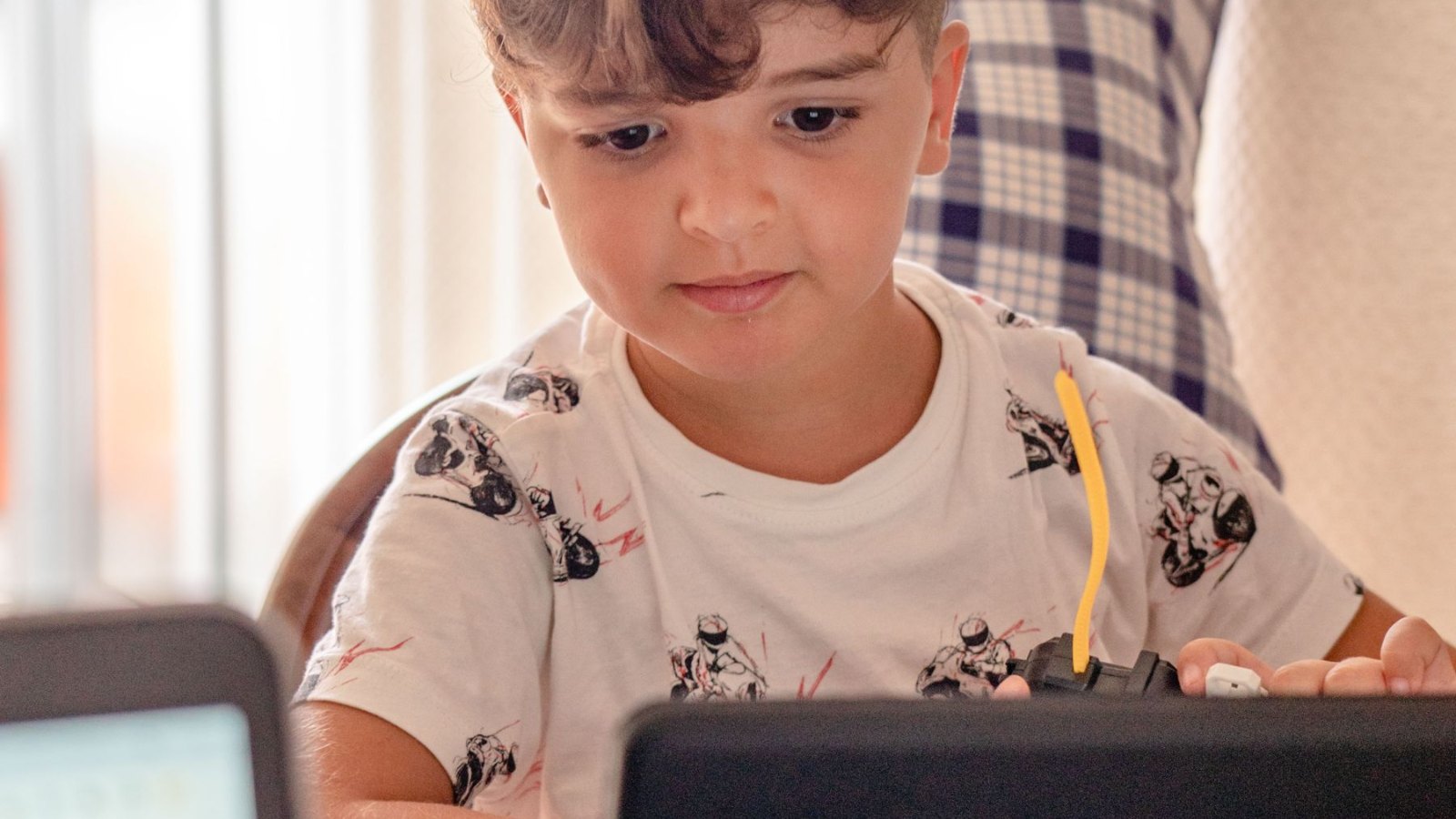 明るい部屋で、ノートパソコンのそばに座って学ぶ子ども