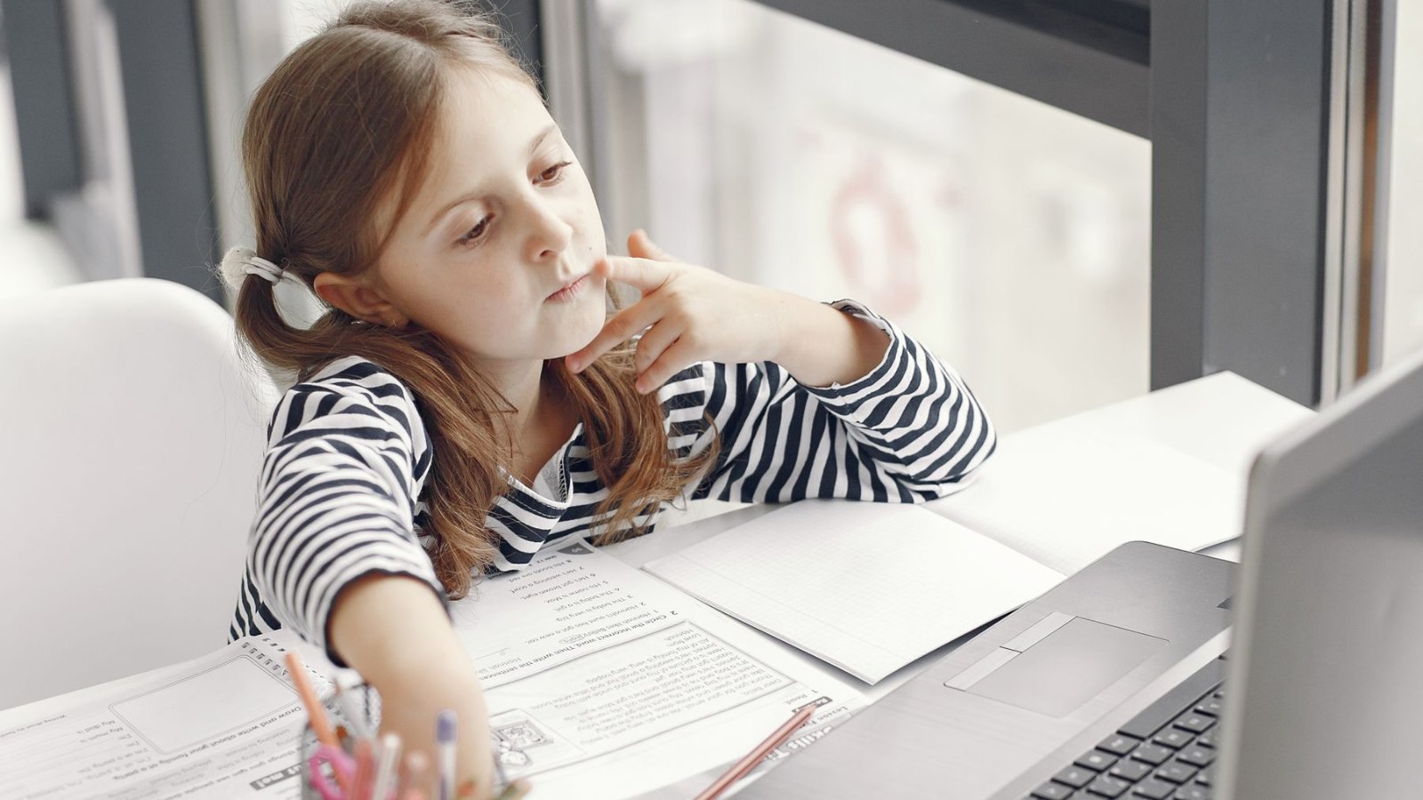 明るい部屋で、ノートパソコンと教科書を広げて学ぶ子ども