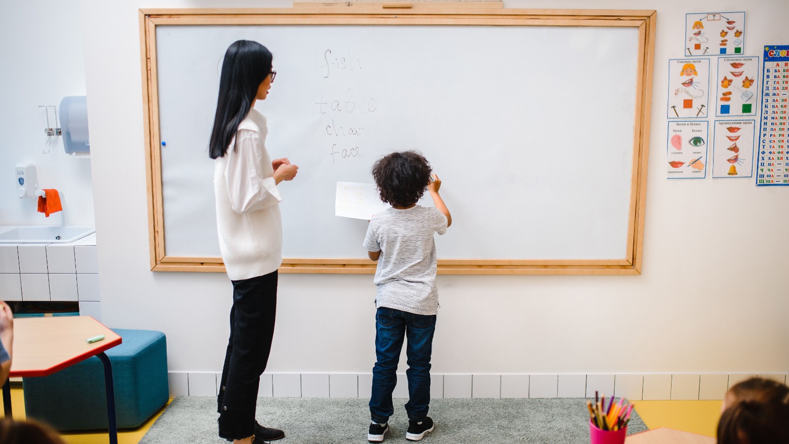 教室で先生と一緒にホワイトボードに英語を書く男の子