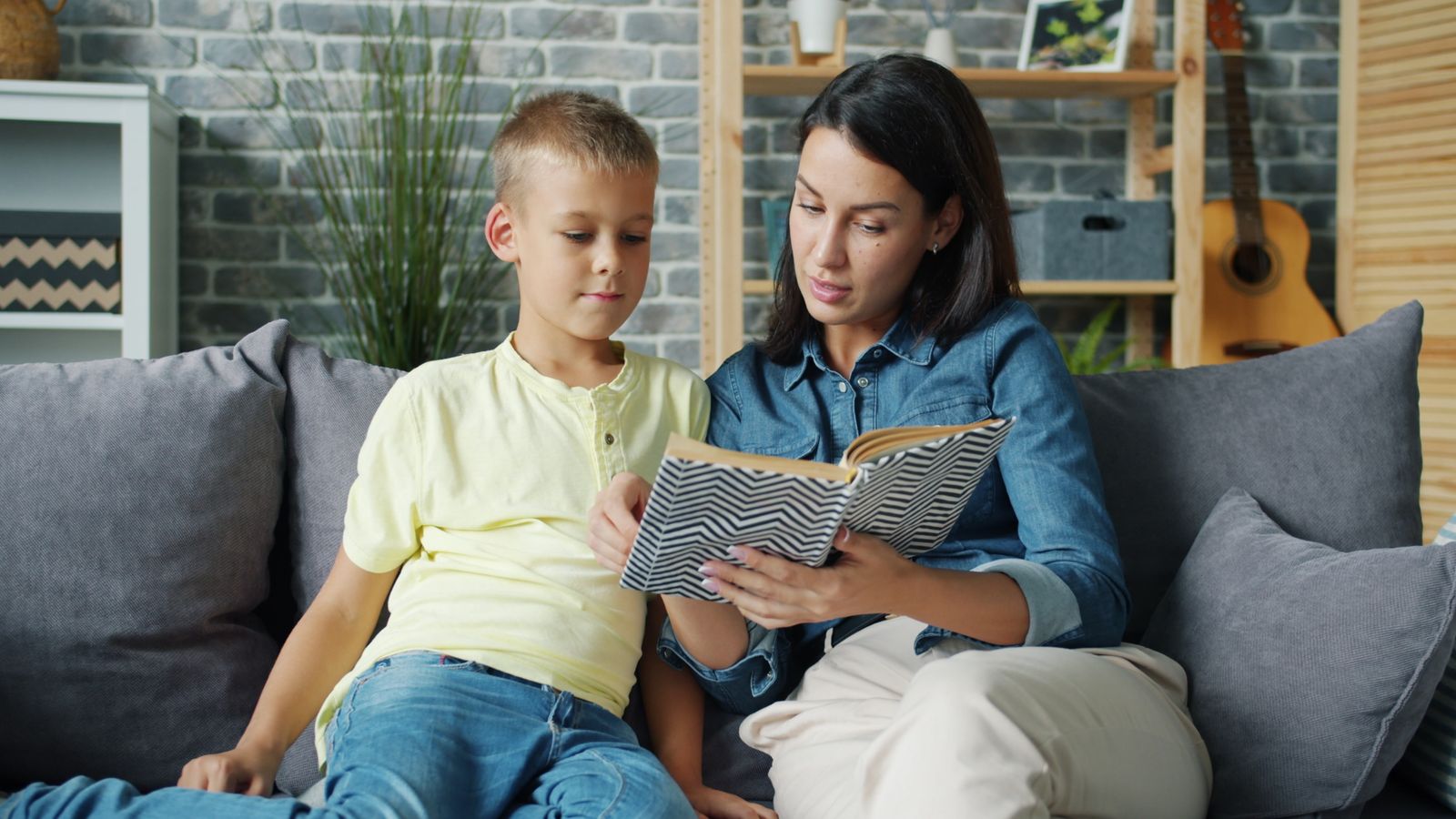 A parent and child reading together on a sofa in the evening