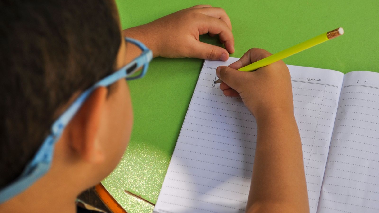 A child writing in a notebook with a pencil at a desk