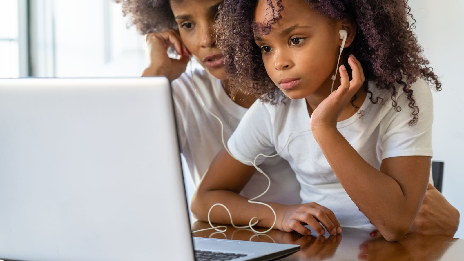 A parent and child sitting together in front of a laptop, both wearing headphones during an online lesson
