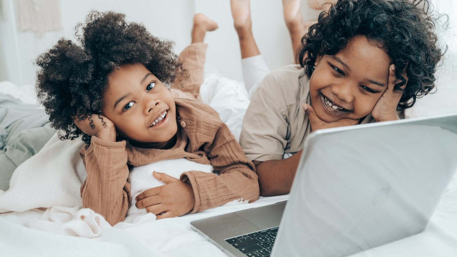 Two children of primary-school age sitting side by side with a laptop, talking and smiling
