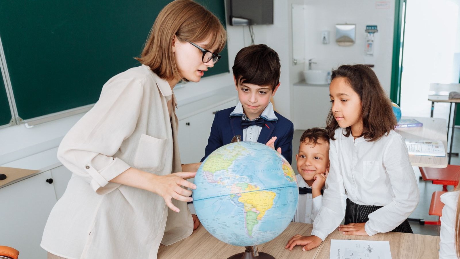 先生と一緒に地球儀を囲んで学ぶ子どもたち