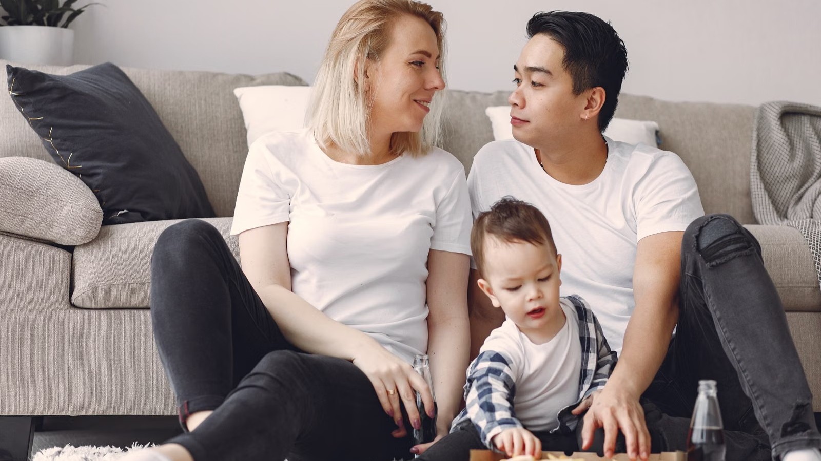 A family of three sitting together on a sofa in a bright living room, talking and smiling
