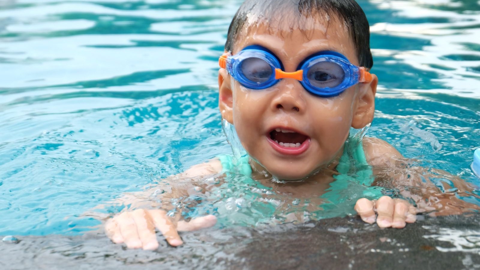 水泳ゴーグルをつけて笑顔でプールにつかる子ども