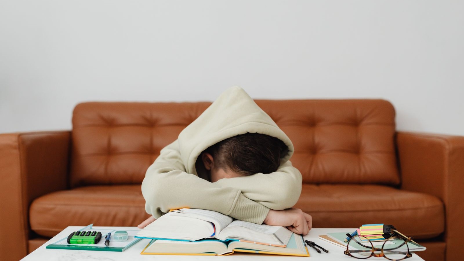 A tired child leaning forward over study materials on a sofa