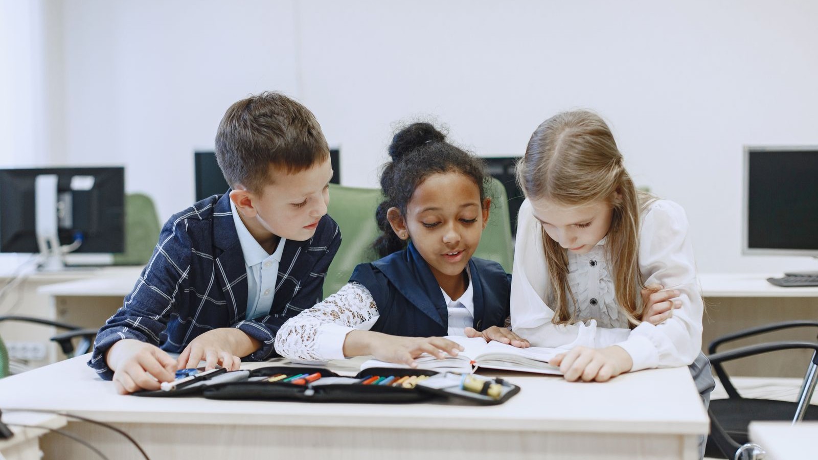 Three children working together at a desk in a classroom