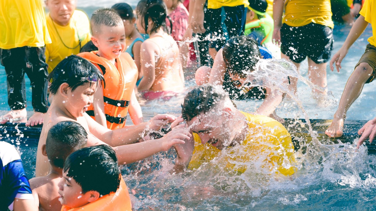 水遊びのレッスンで先生と一緒に水しぶきを上げる子どもたち