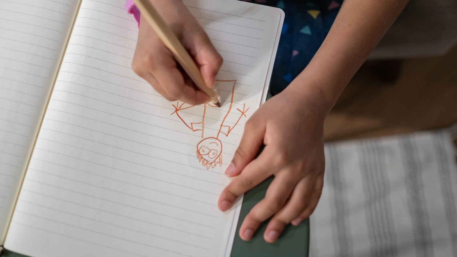 机の上のノートに絵を描く子どもの手元