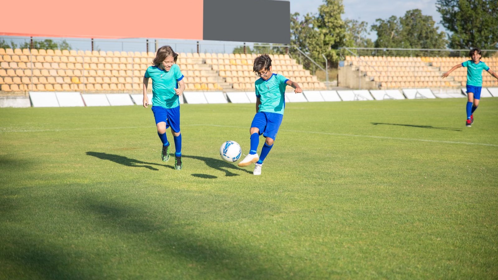 スタジアムの芝の上でサッカーのボールを追う子どもたち