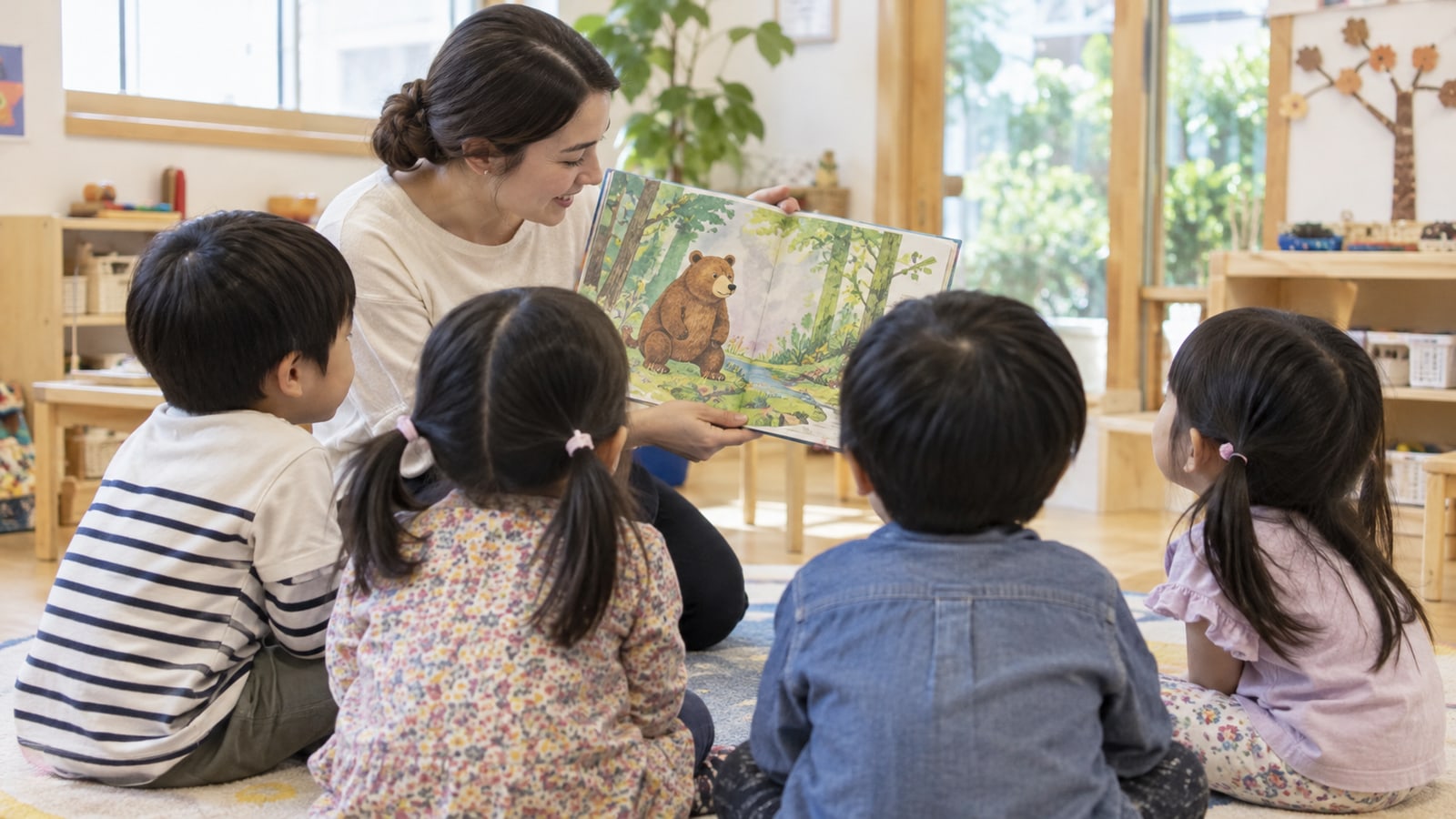 明るい保育室で先生と子どもたちが絵本を囲む様子