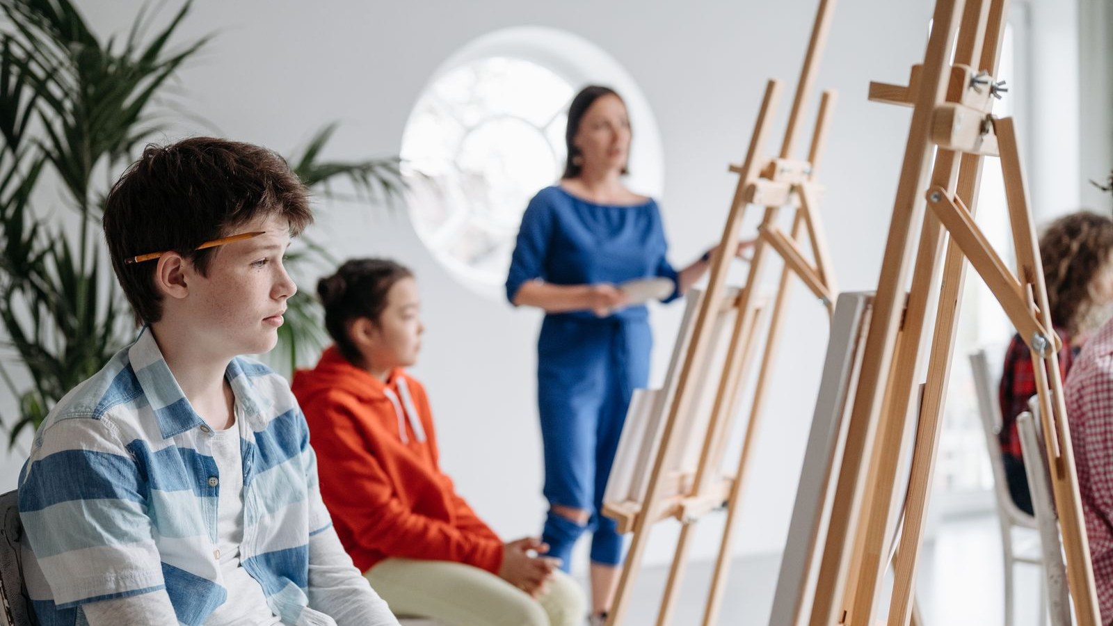 イーゼルの前で先生の話を聞きながら絵を描く教室の子どもたち