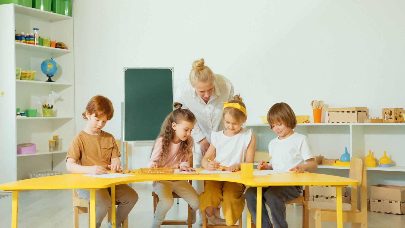 明るい教室で先生に教わる子どもたち