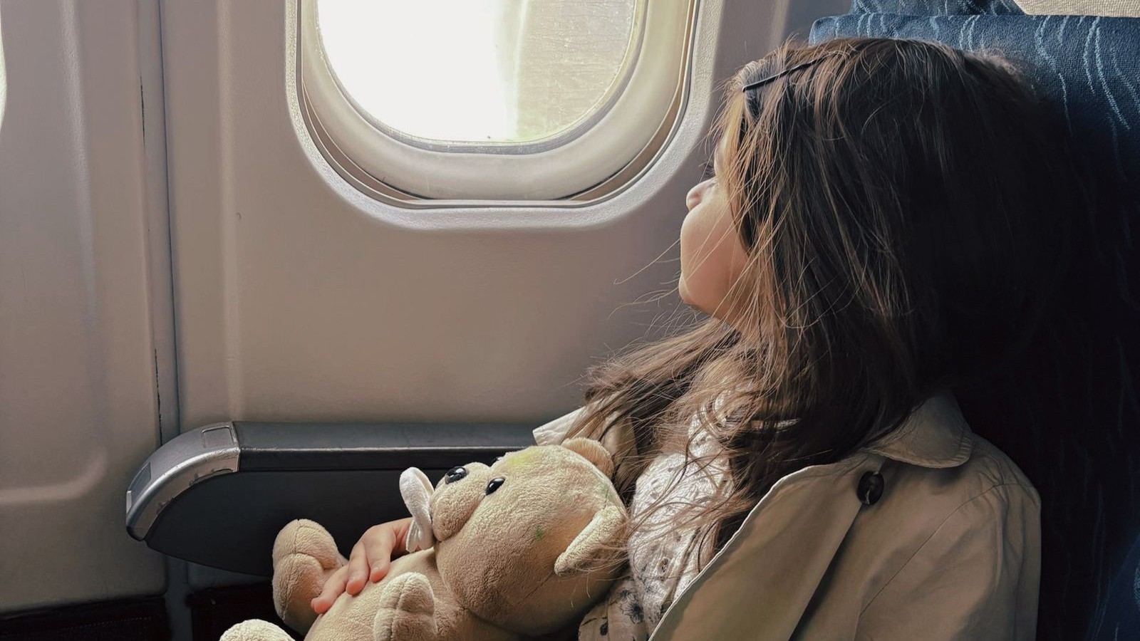 A girl sitting beside an aeroplane window holding a soft toy