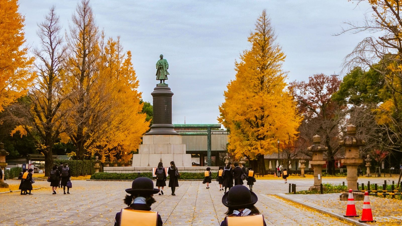 Two children with Japanese school backpacks walking along a tree-lined avenue