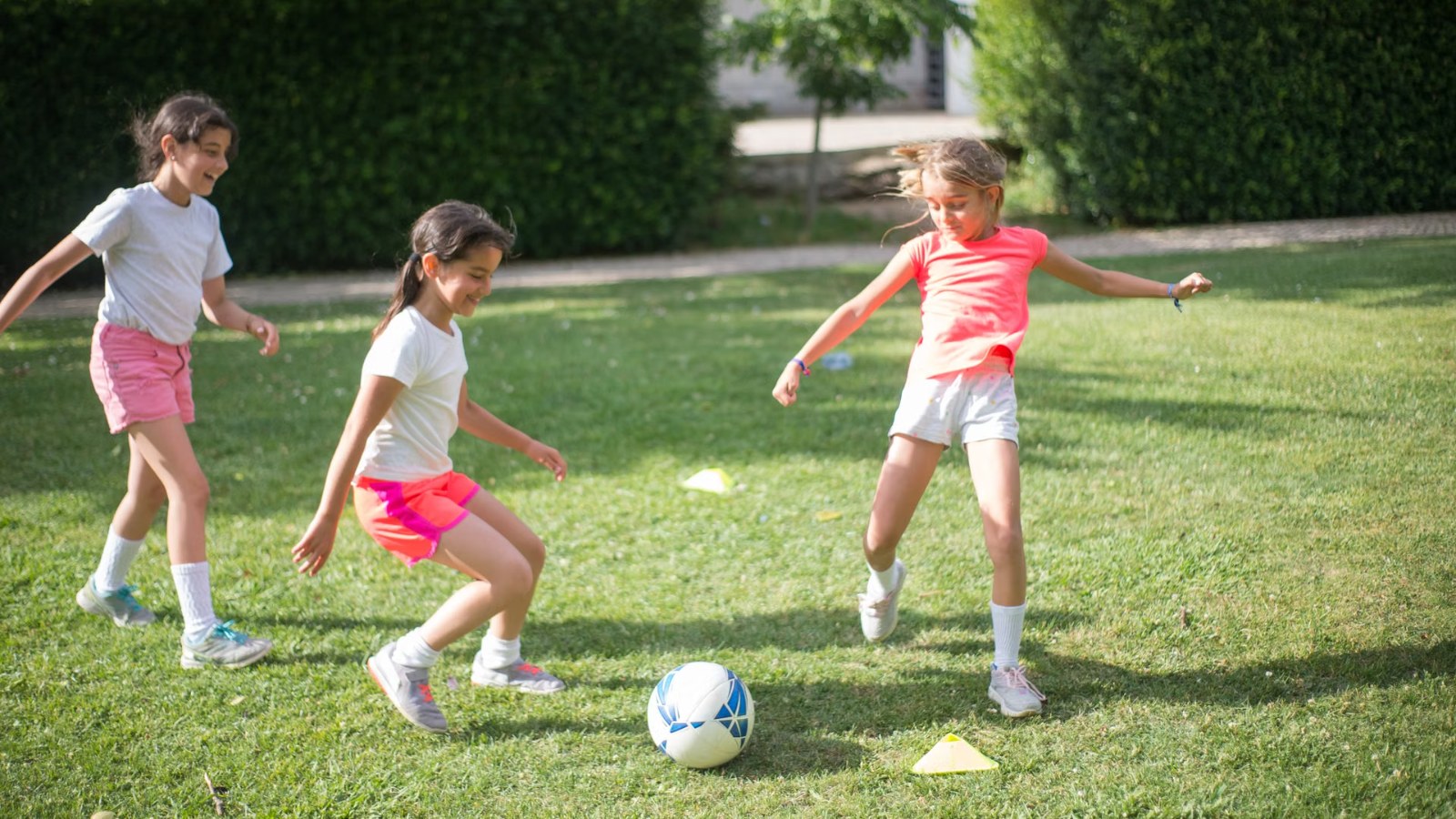 芝生のグラウンドでボールを追いかけてサッカーを楽しむ3人の女の子