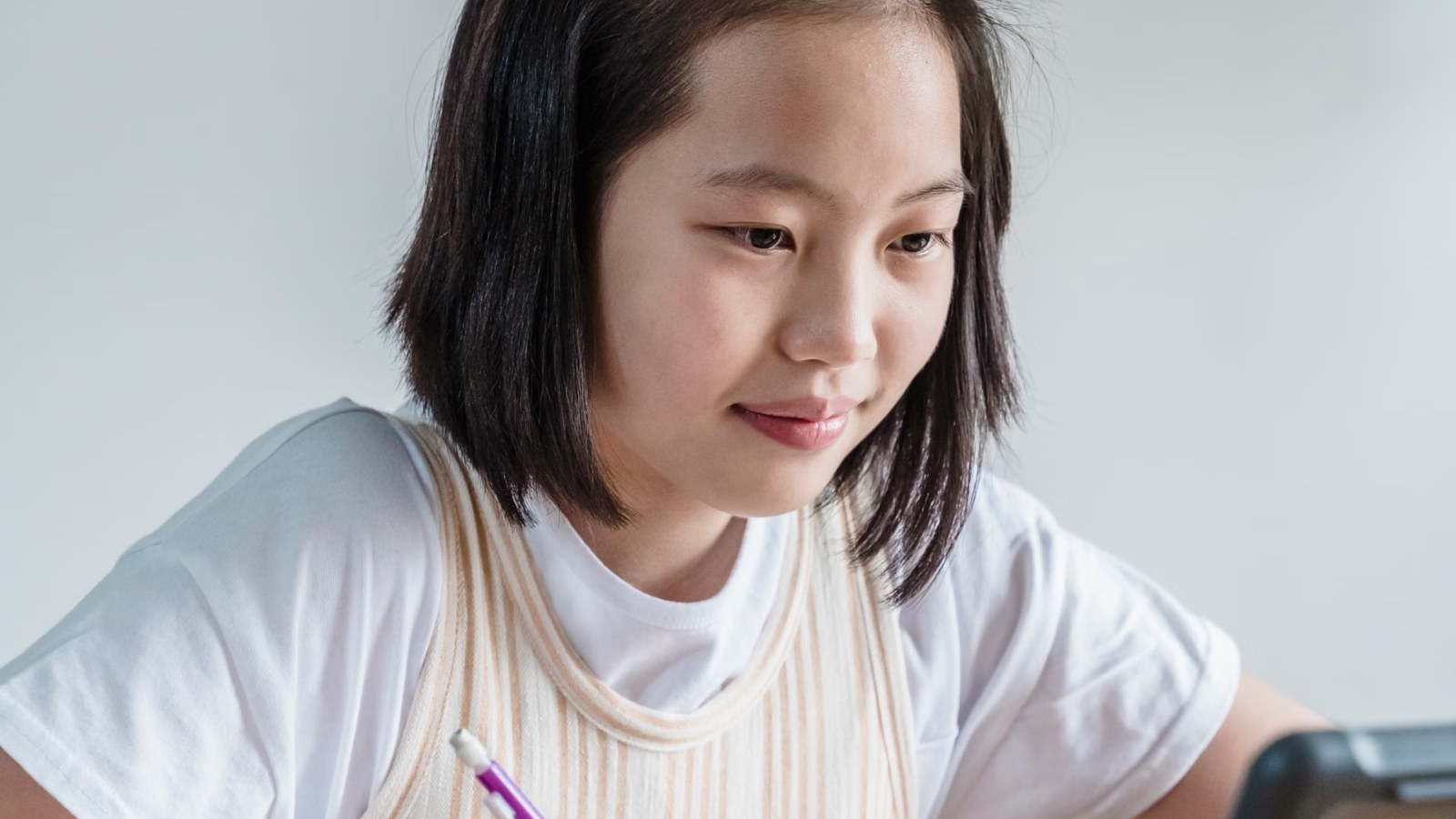 タブレットを使い、自宅でノートを広げてオンラインで学ぶ女の子