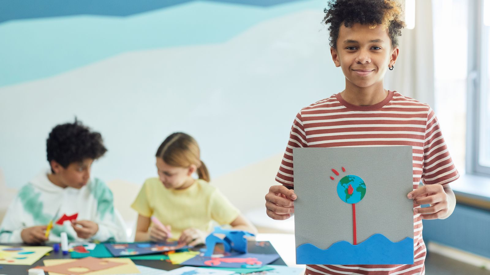 工作で作った作品を見せる子どもと、制作する仲間