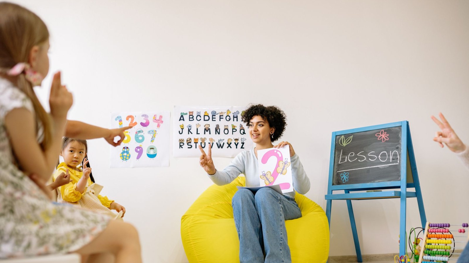 アルファベットや数字が貼られた教室で、先生と一緒に学ぶ子どもたち