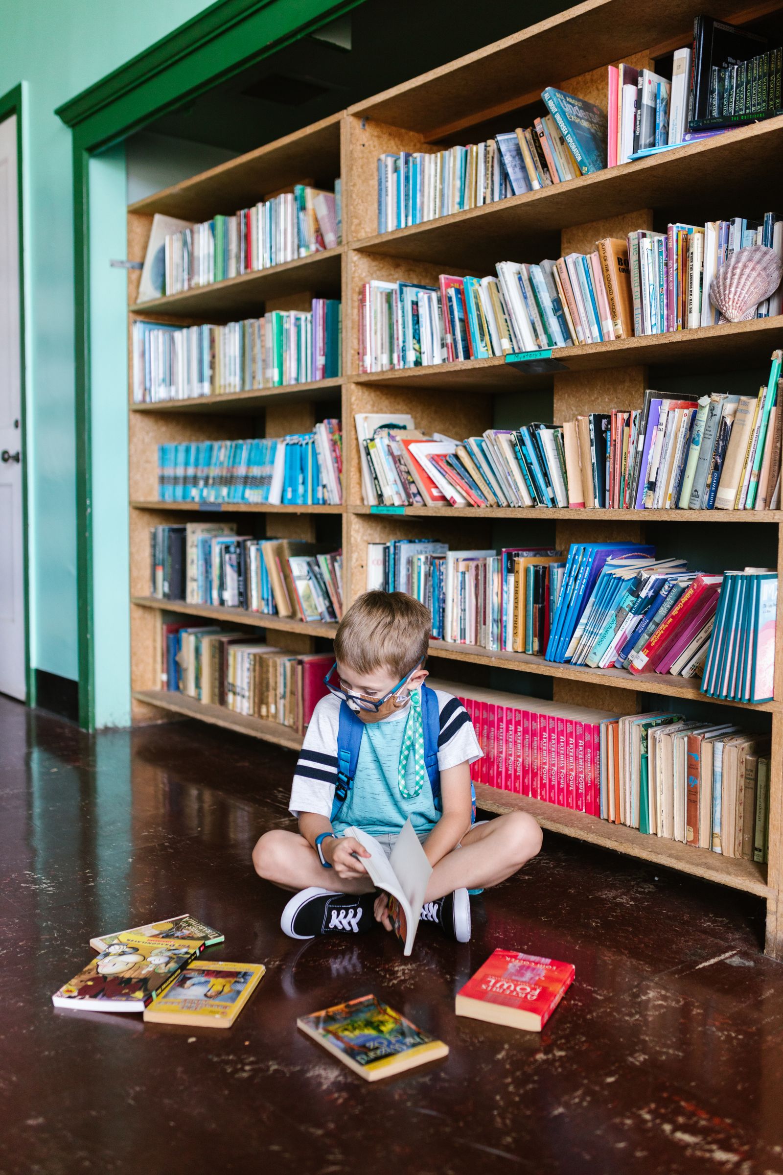 図書館の本棚の前で本を読む男の子