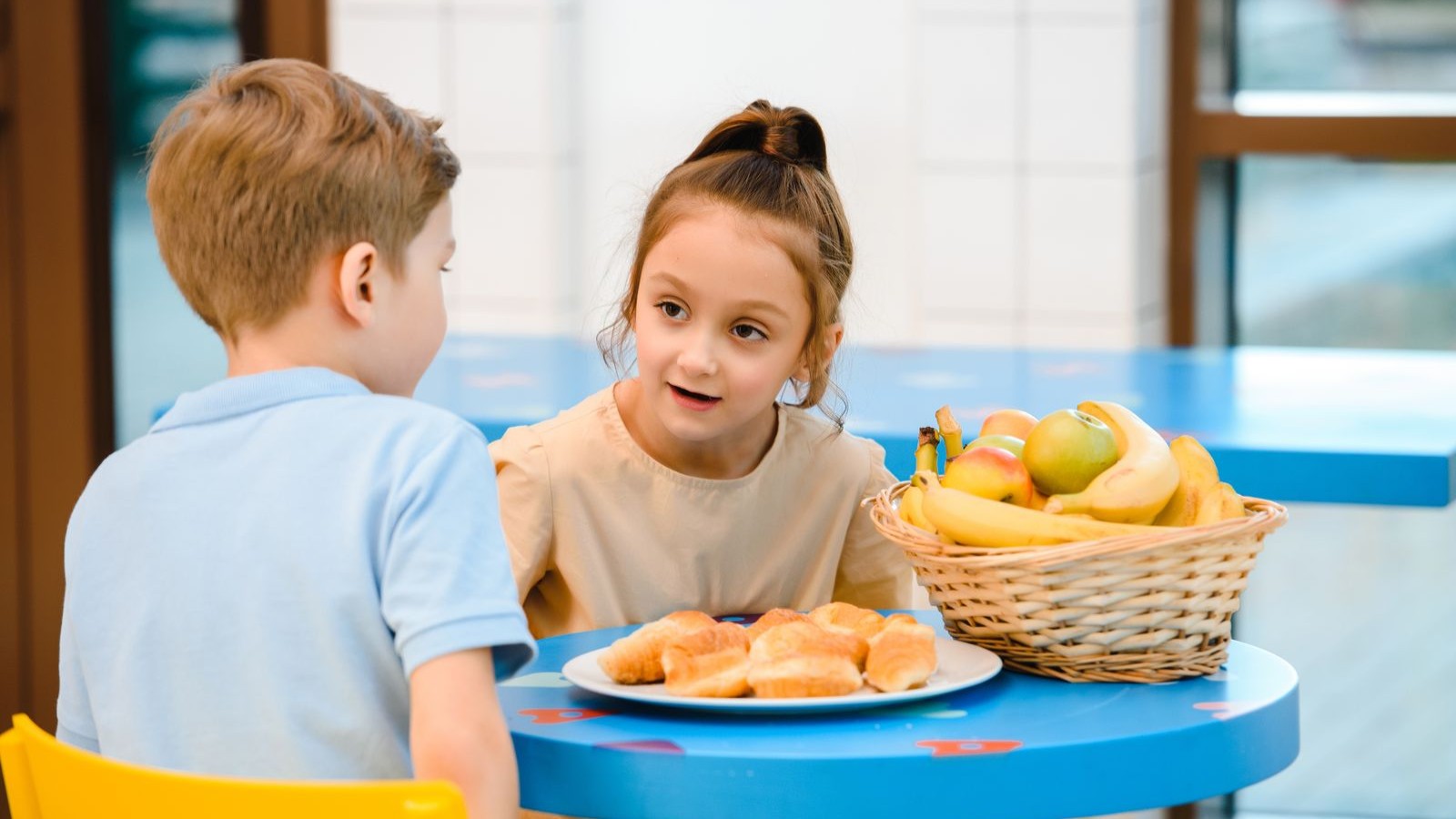 Two young children sitting together at a low table, talking and drawing