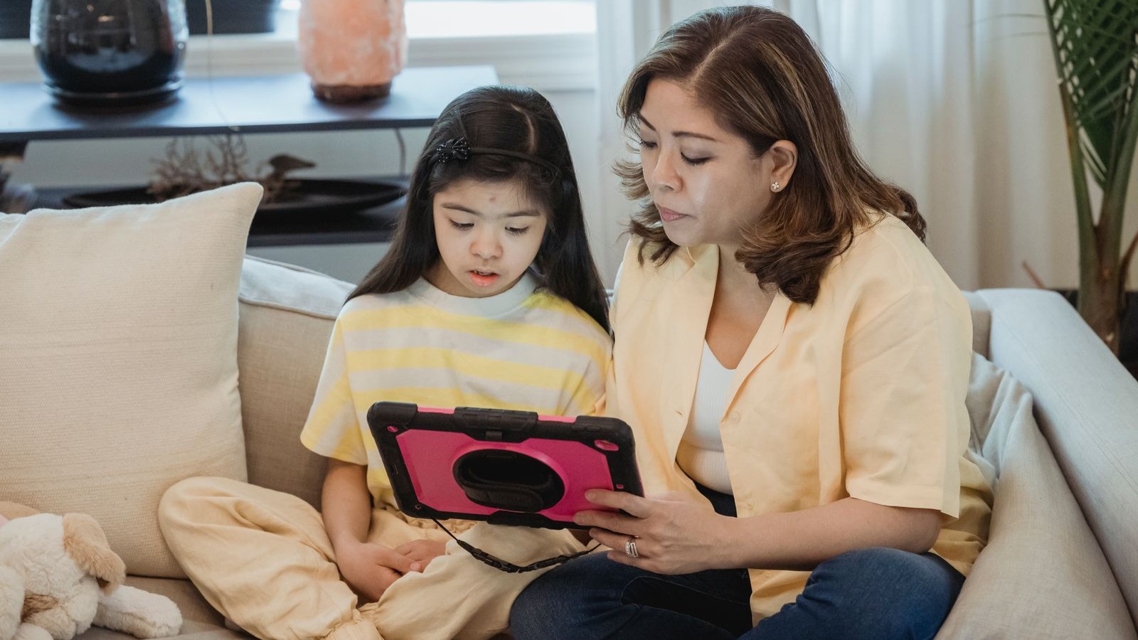 A parent and child looking at a tablet together on a sofa