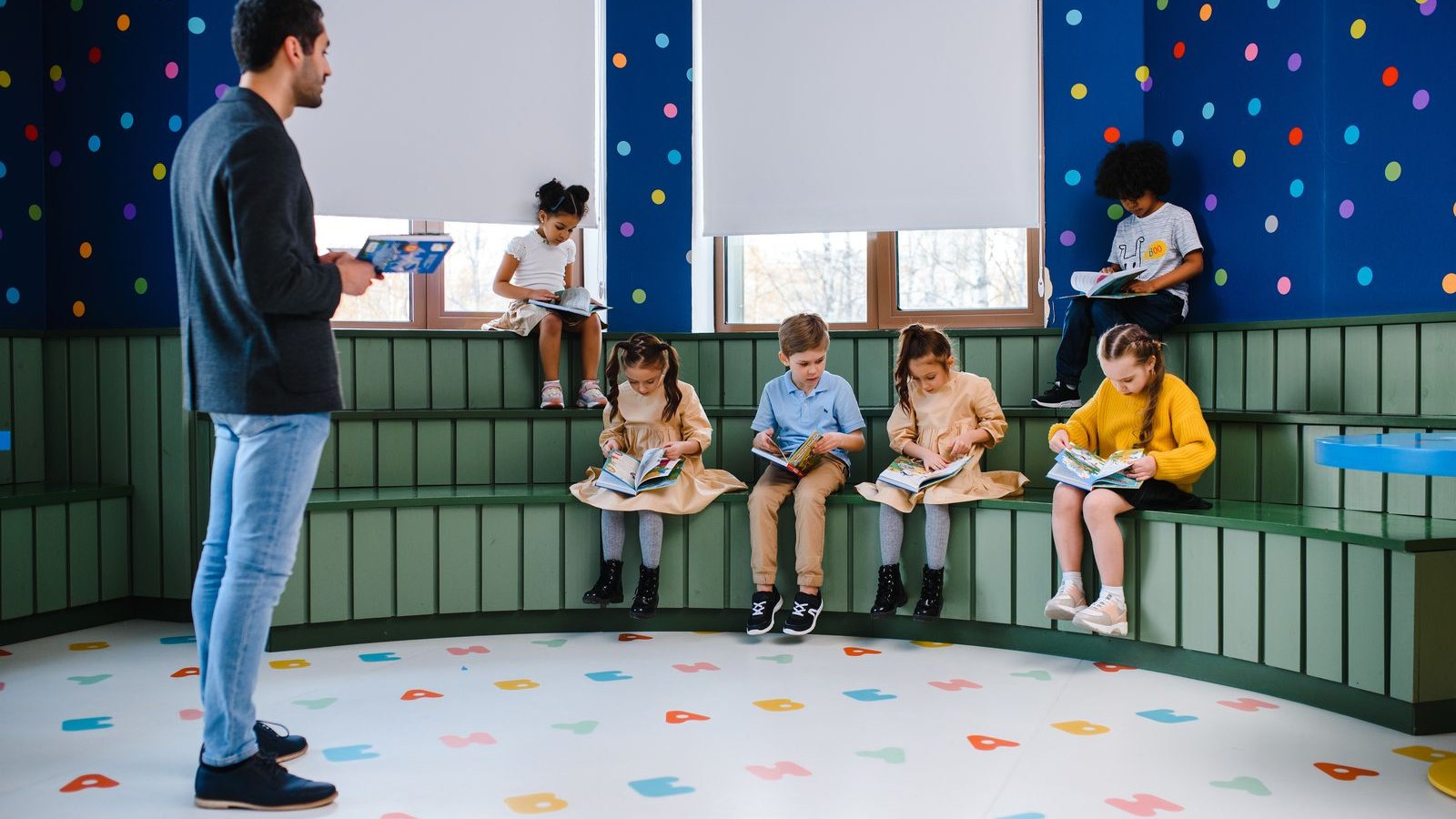 先生の読み聞かせを、部屋の階段状の席で聞く子どもたち