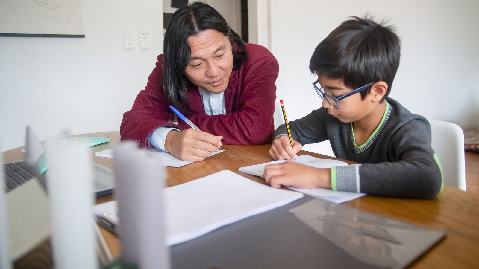 先生と並んで机に向かい、ノートに書きながら勉強する男の子