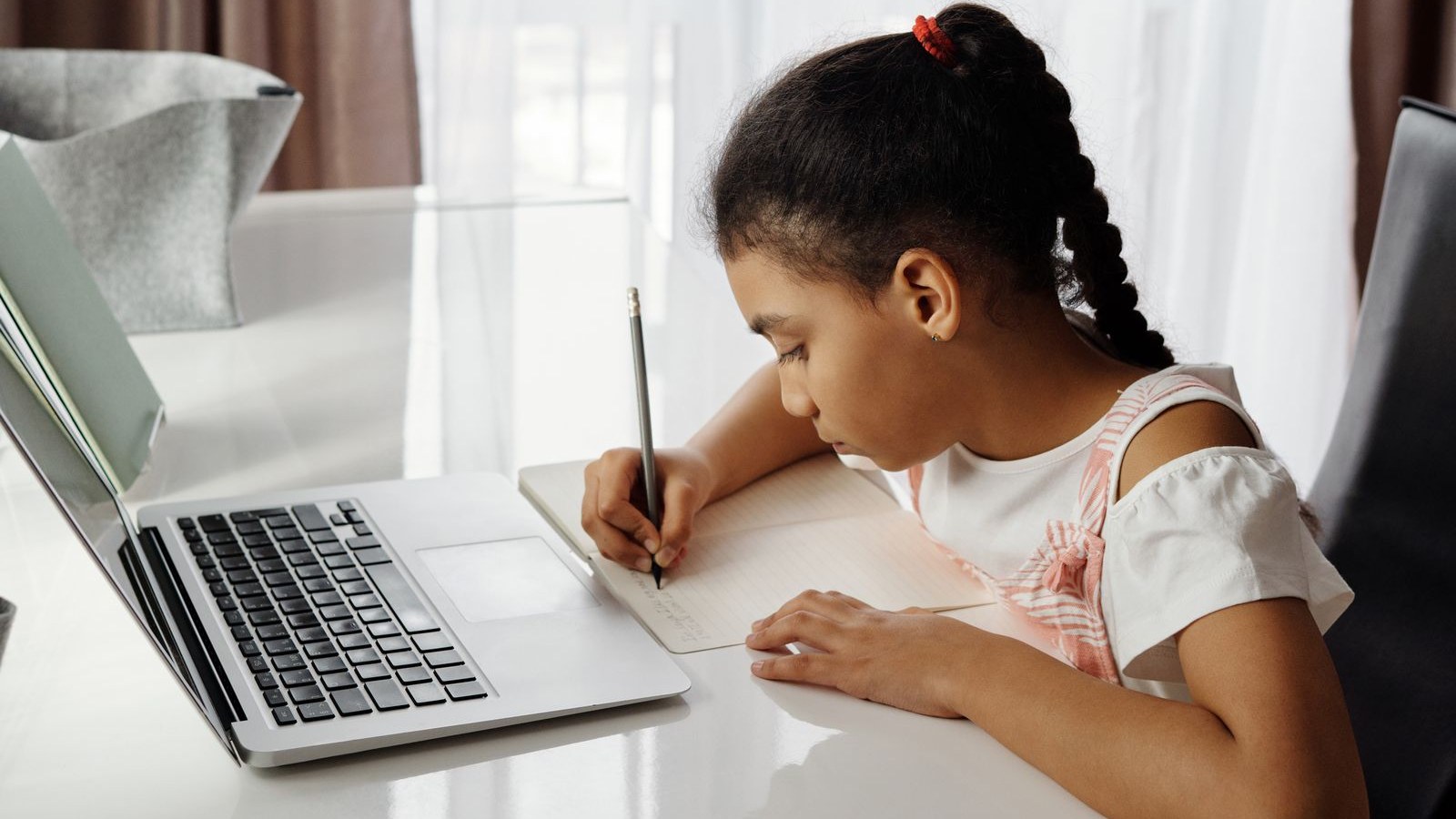 自宅でノートパソコンを前に、鉛筆で書き込みながらオンラインで学ぶ女の子