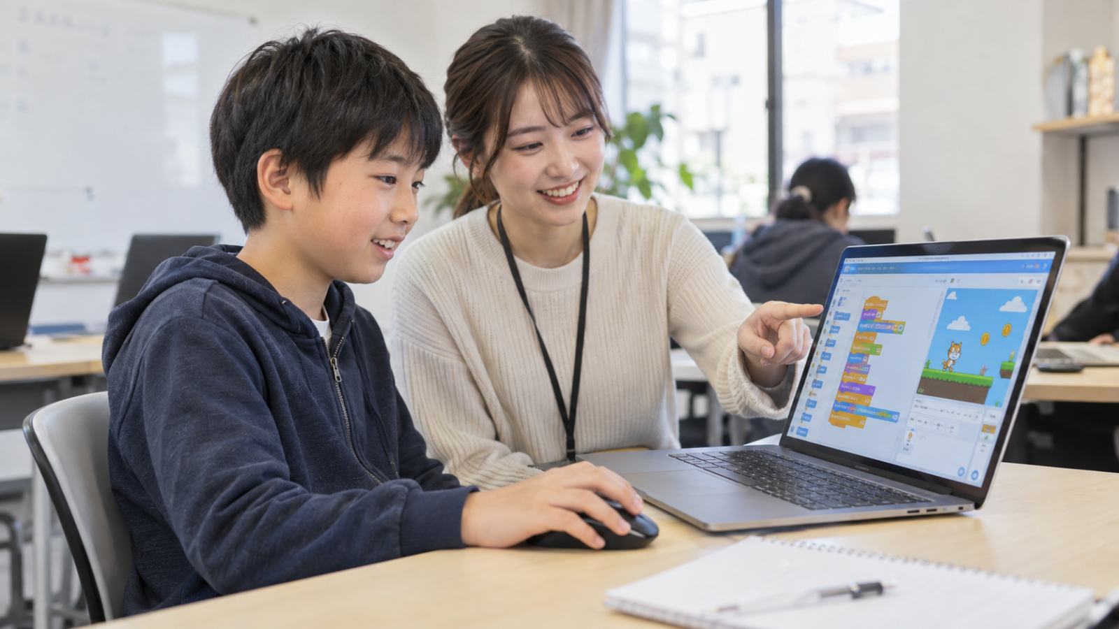 先生の説明を受けながらパソコンでゲームのプログラミングに取り組む子ども（AI生成のイメージ）