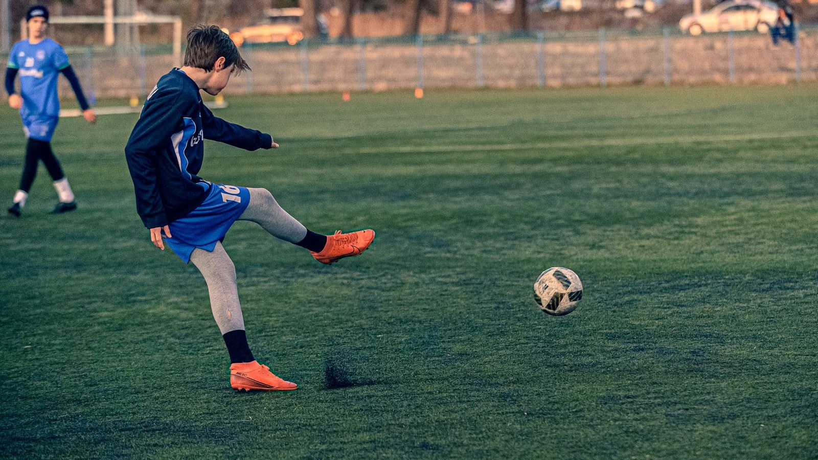 芝のグラウンドでサッカーのボールを蹴る子ども