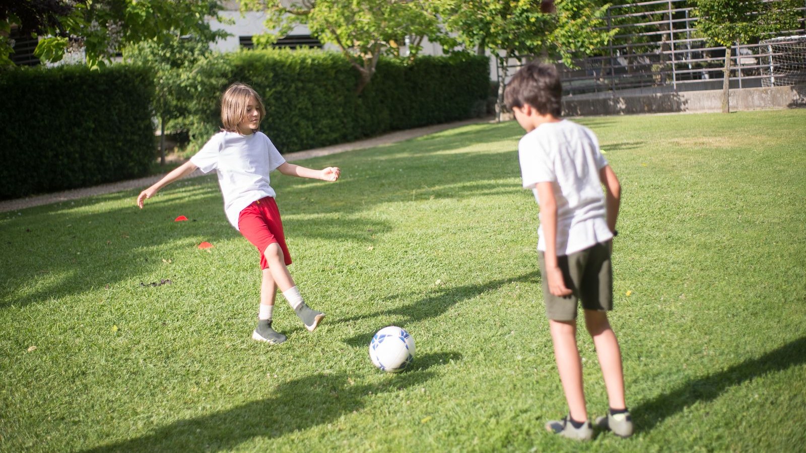 公園のグラウンドでボールを蹴って遊ぶ子どもたち（サッカーのイメージ）