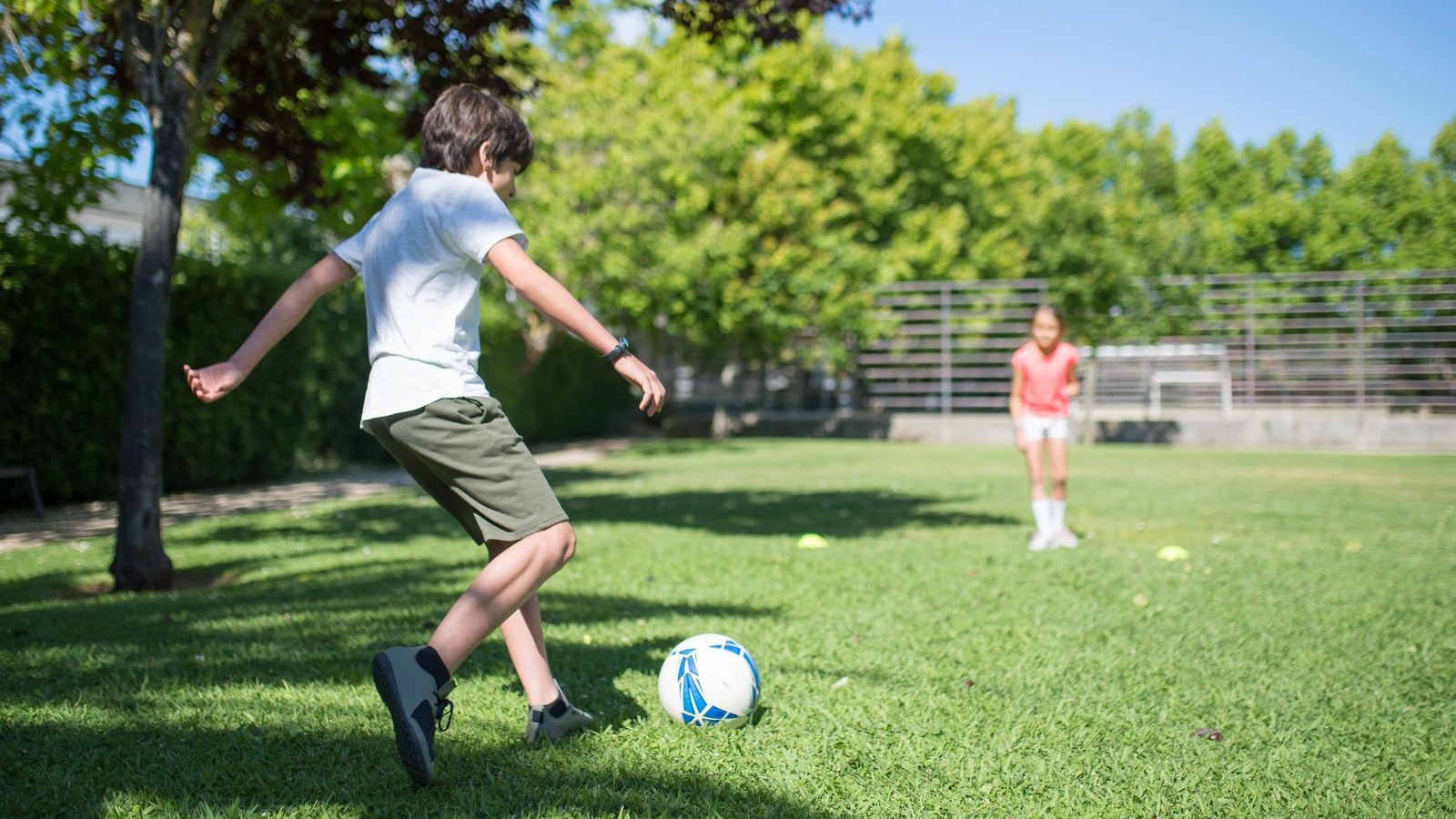 芝生のグラウンドでサッカーボールを蹴る子ども