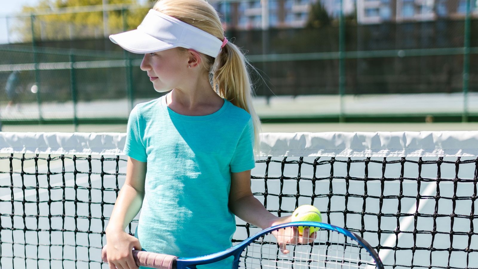 テニスコートでラケットとボールを持つバイザー姿の子ども