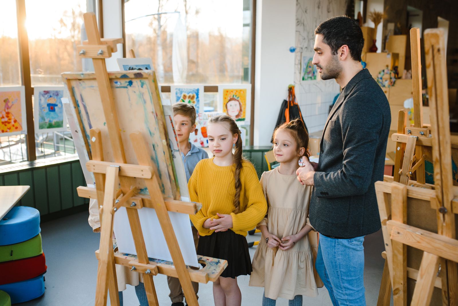 先生のそばで、イーゼルに向かって絵を学ぶ子どもたち