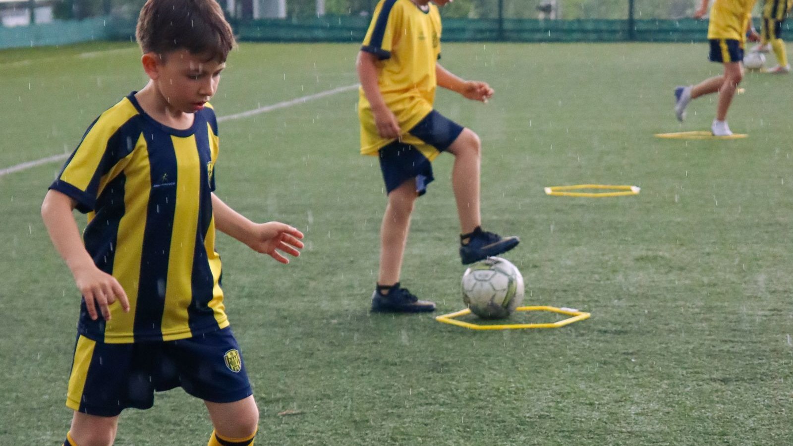 コーチのそばでサッカーのドリブル練習をする子ども