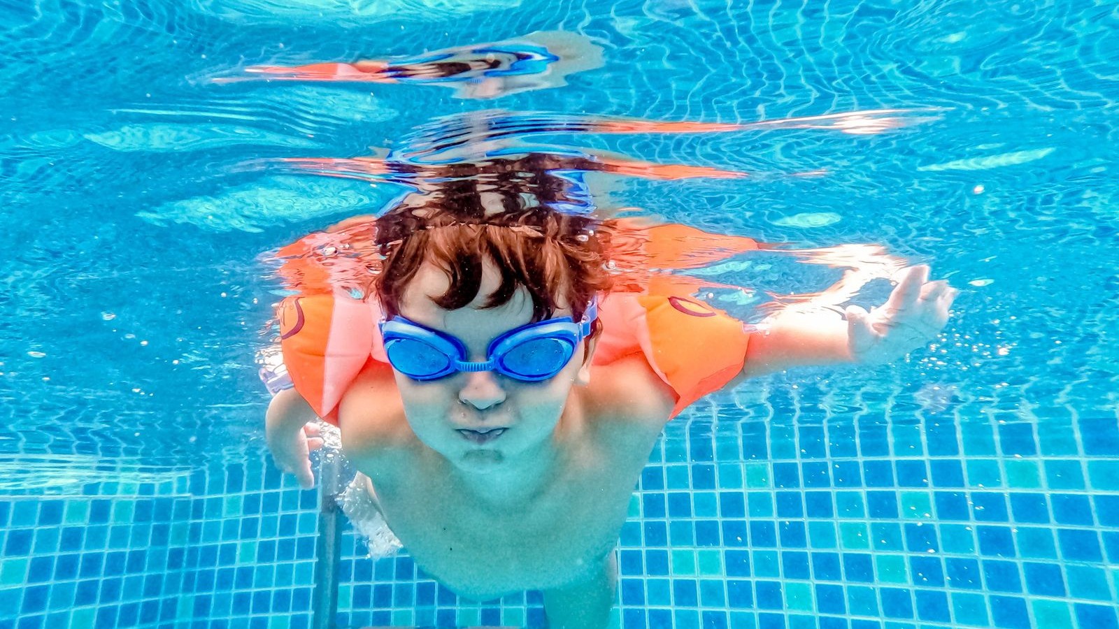 青いゴーグルをつけてプールで泳ぐ男の子