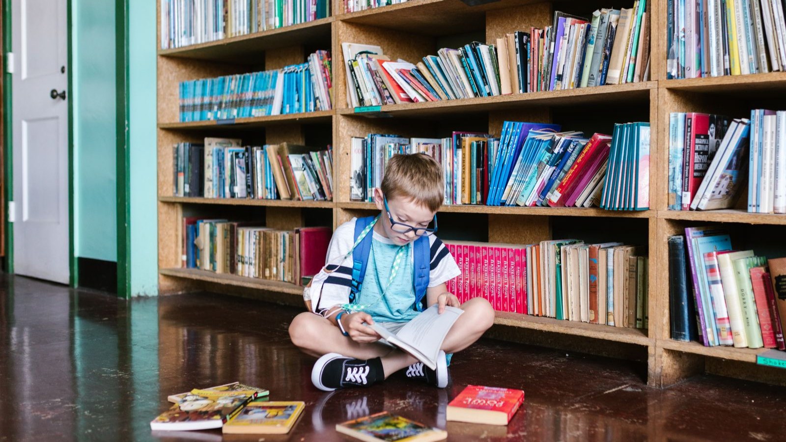 図書館の本棚の前で本を読む男の子