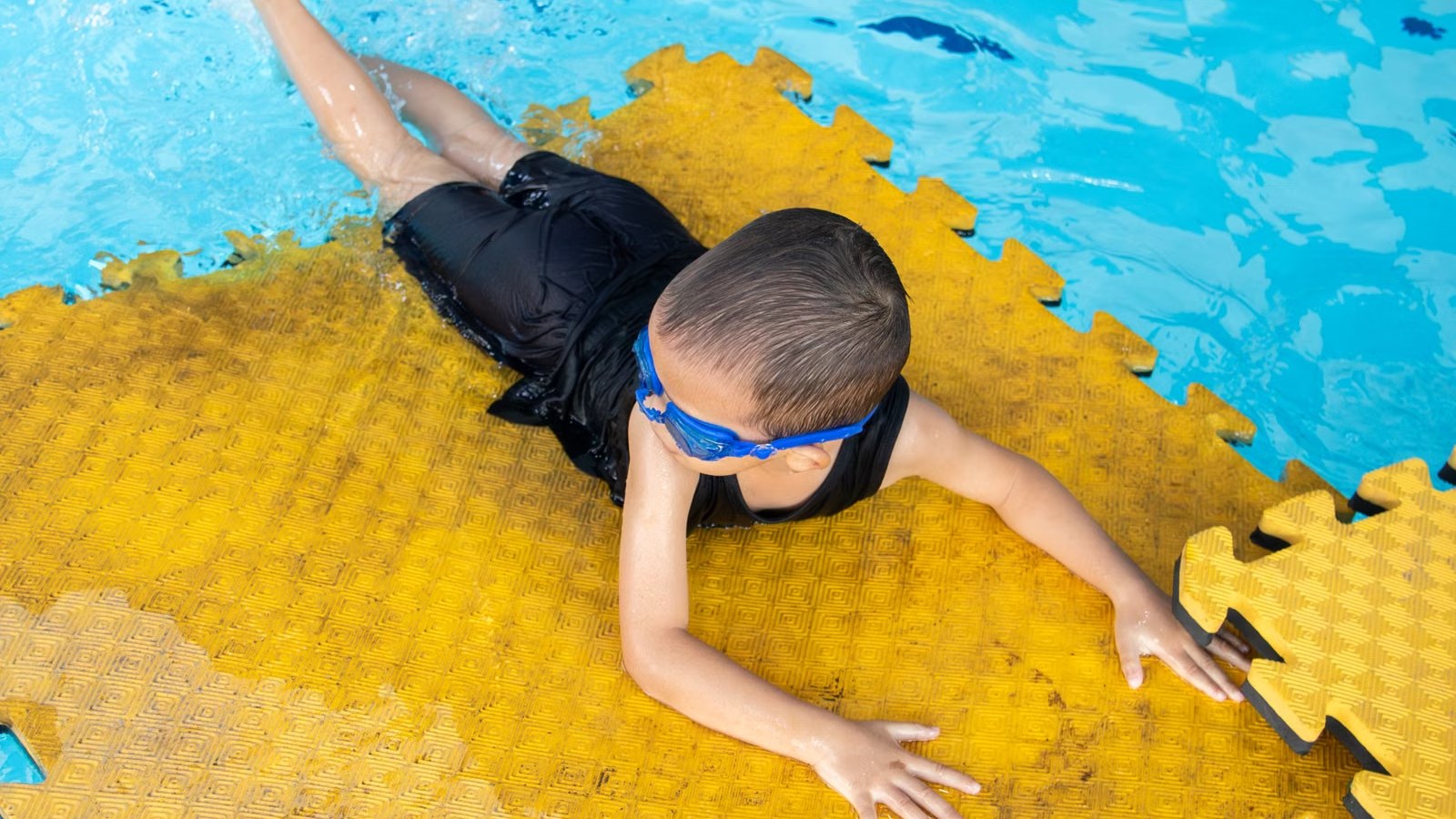 プールでマットにつかまって水泳の練習をする子ども